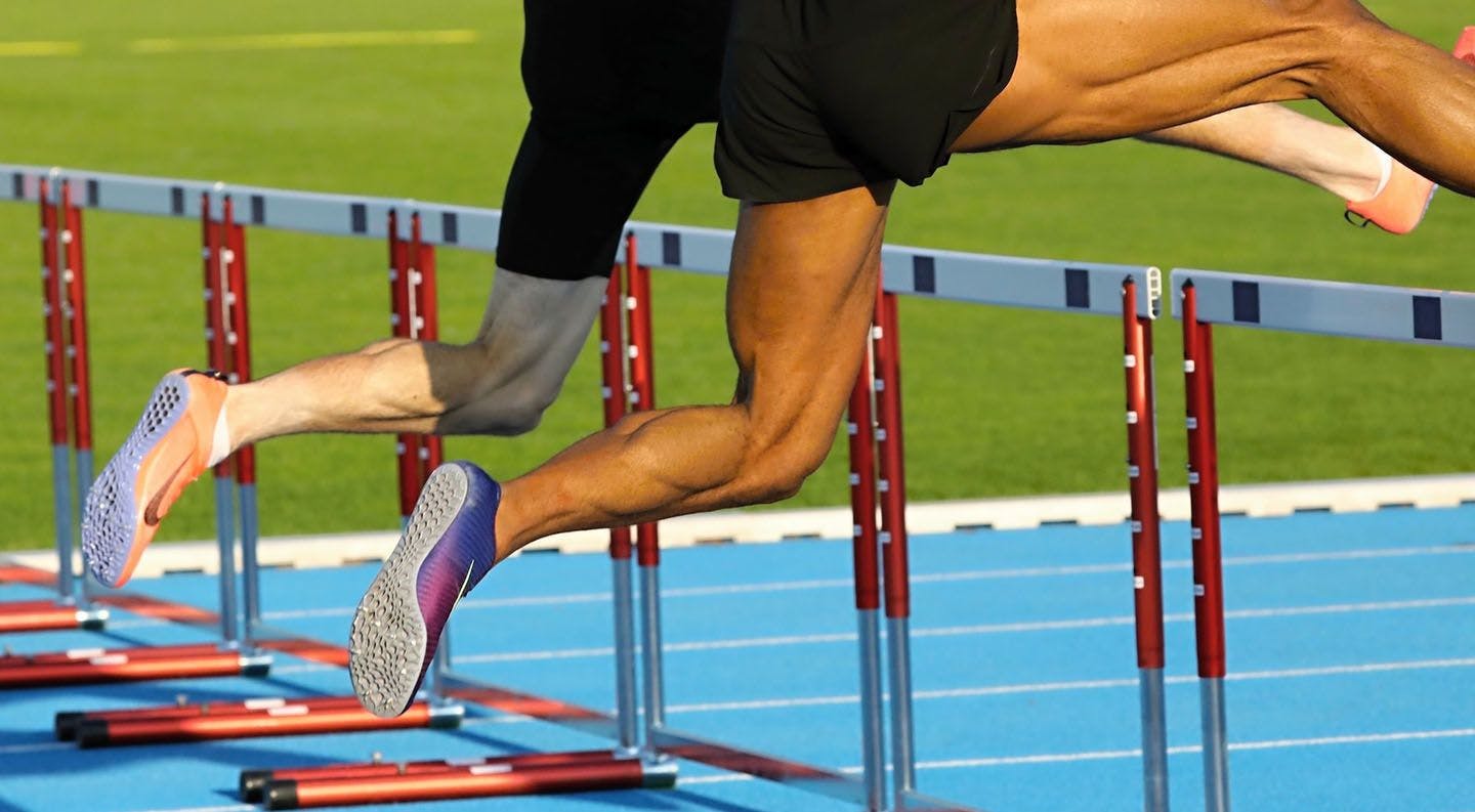 Two athletes jumping over some hurdles 
